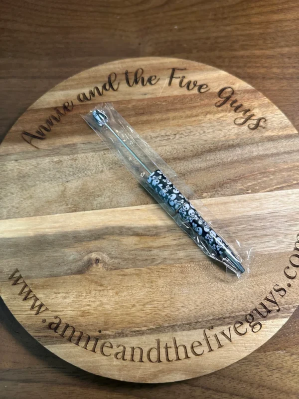 A Printed Beadable pen in plastic packaging is placed on a round wooden board with "Annie and the Five Guys" and a web address engraved on it.