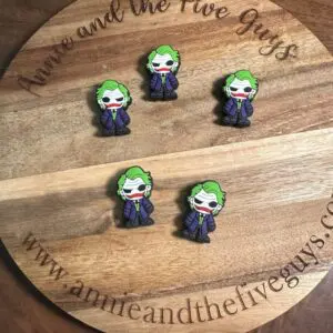 Five Jokster silicone focal beads featuring a cartoon figure with green hair and a purple suit are displayed on a round wooden board. The board has text that reads "Annie and the Five Guys" and a website URL.