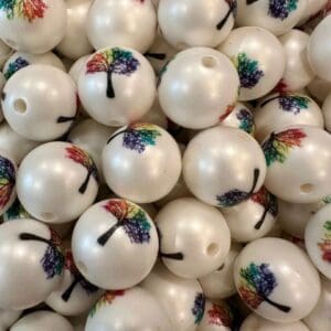 A pile of white spherical beads with colorful tree designs printed on them, featuring a hole for stringing.