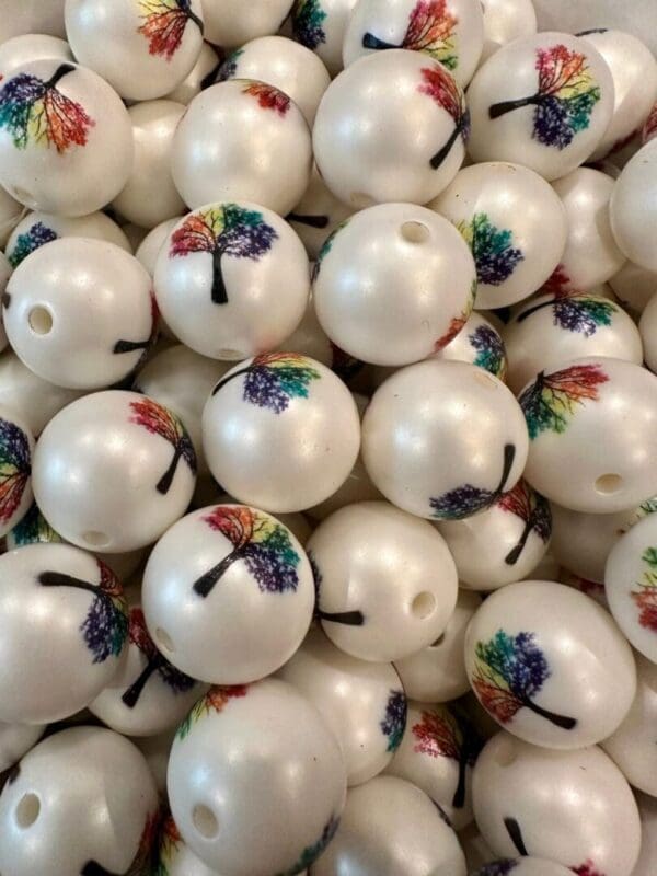 A pile of white spherical beads with colorful tree designs printed on them, featuring a hole for stringing.