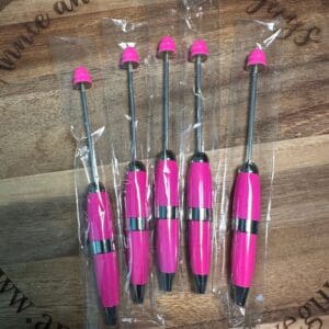 Five pink arrow fletching tools on a wooden surface with plastic wrapping.