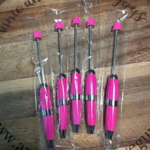 Five pink arrow fletching tools on a wooden surface with plastic wrapping.