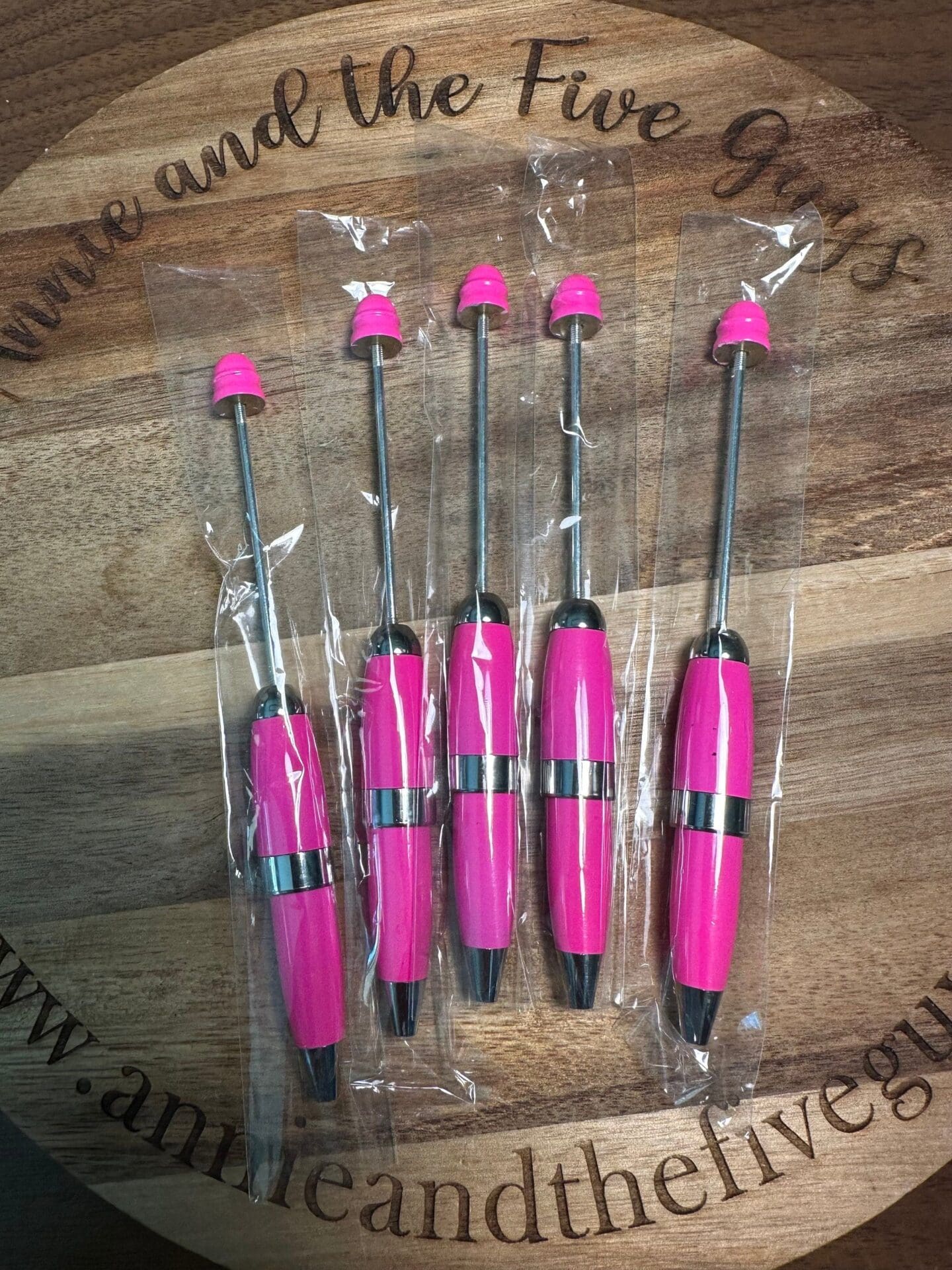 Five pink arrow fletching tools on a wooden surface with plastic wrapping.