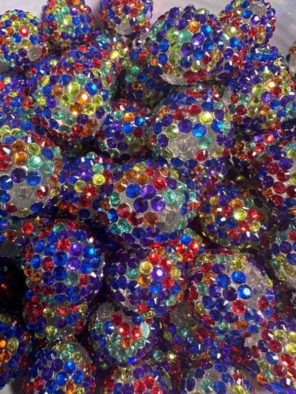 A close-up image of numerous decorative balls covered in colorful, multi-faceted gems in various shades of blue, red, green, yellow, and purple.