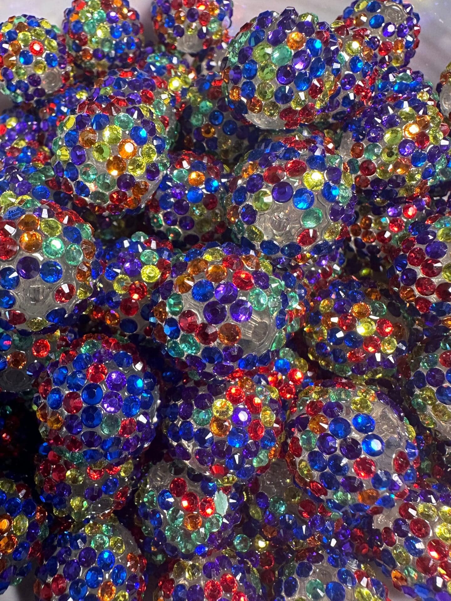 A close-up image of numerous decorative balls covered in colorful, multi-faceted gems in various shades of blue, red, green, yellow, and purple.