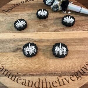 Wooden board with the words "Annie and the Five Guys" engraved, displaying black and white decorative items featuring chandelier designs. A silver writing instrument is also on the board.