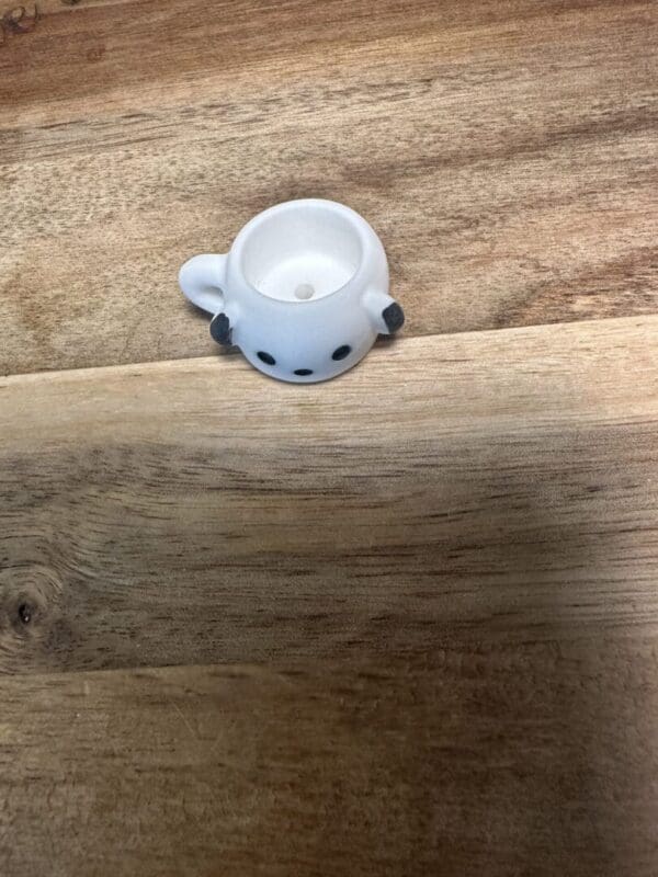 A small, white Sanrio cups resin bead with black dots resembling eyes and ears sits on a wooden surface.