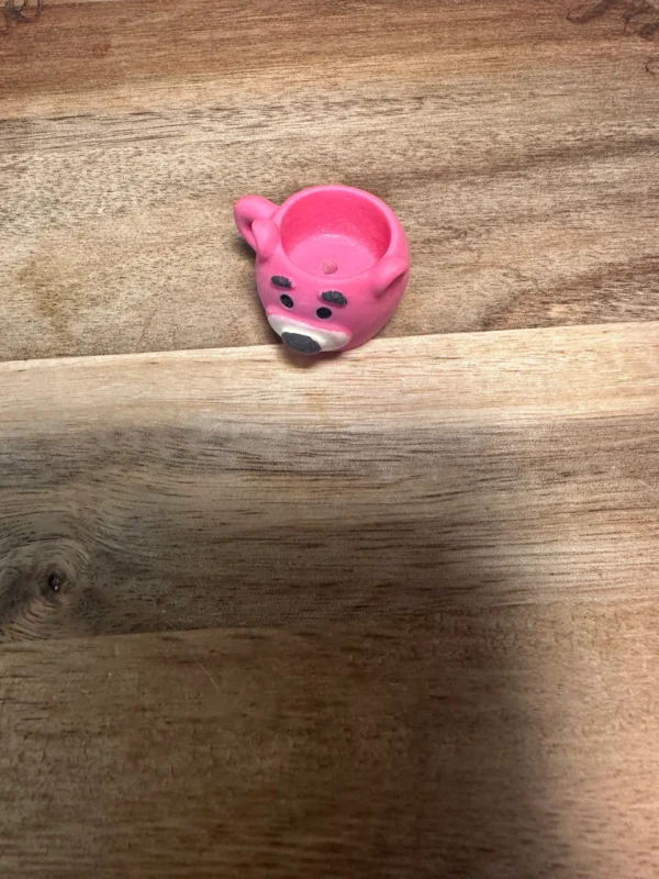 A small pink Sanrio cups resin bead shaped like a bear's face sits on a wooden surface.