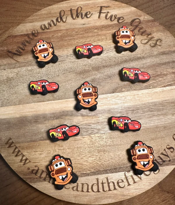 Colorful cartoon truck or car silicone focal beads arranged on a wooden board with "Annie and the Five Guys" written on it.