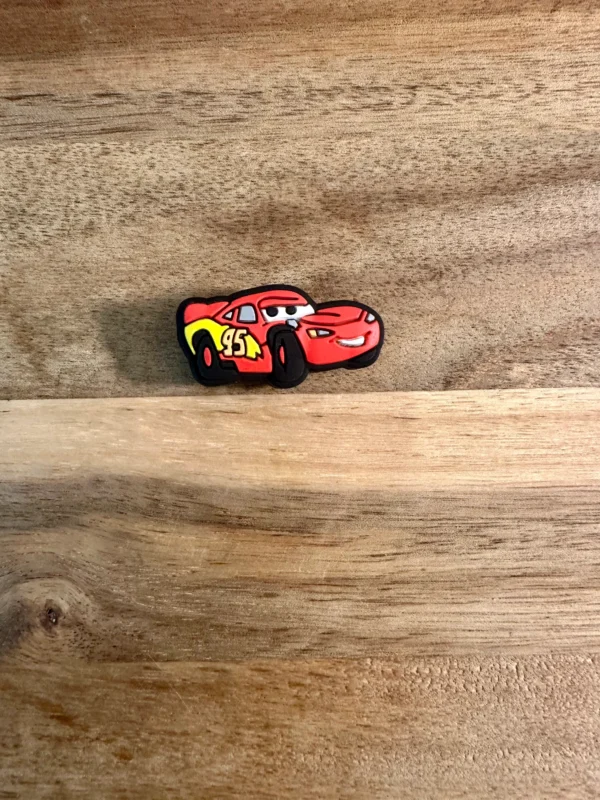 A small Cartoon truck or car silicone focal bead resembling a race car with eyes and a smile is placed on a wooden surface.