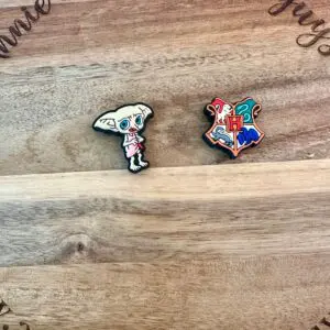 Two HP silicone focal beads displayed on a wooden surface; one is shaped like a small creature with large ears, and the other is a multicolored crest. Text on the wood reads "Annine and the Five Guys.