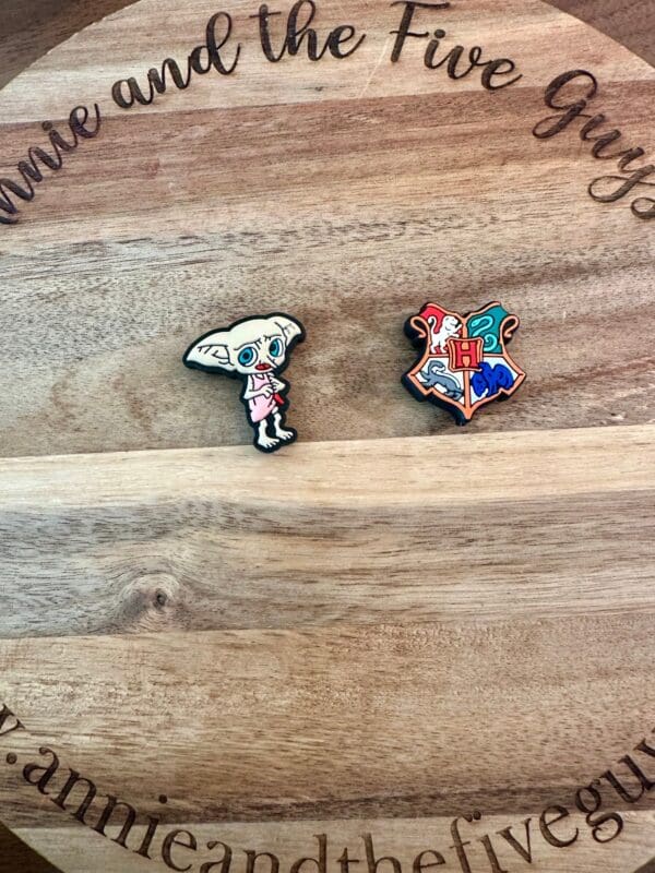 Two HP silicone focal beads displayed on a wooden surface; one is shaped like a small creature with large ears, and the other is a multicolored crest. Text on the wood reads "Annine and the Five Guys.