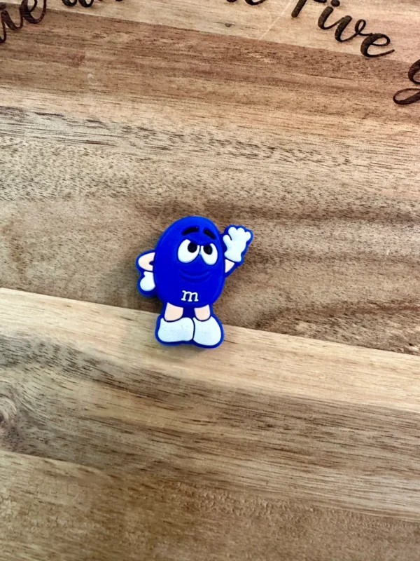 A small plastic figure of the Candy silicone focal bead waving, placed on a wooden surface.