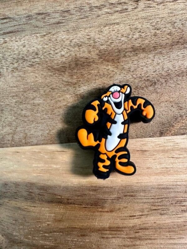 A Honey bear or tiger silicone focal bead featuring an animated tiger character smiling and raising its arms, set against a wooden background.