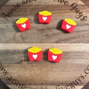 Four small fry-shaped objects with red containers and heart designs are placed on a wooden board engraved with "Sam horror guy silicone focal bead (Copy)" and a website URL.