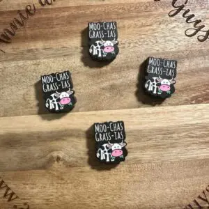 Four "Moo-Chas Gracias" enamel pins shaped like cows with the text "MOO-CHAS GRASS-IAS" are displayed on a round wooden surface with "Annie and the Five Guys" engraved around the edge.