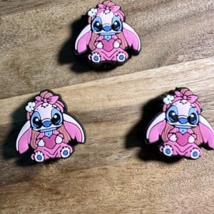 Three identical Little Pink Aliens with blue bows are arranged on a wooden surface. The aliens have large eyes and flowers on their heads.