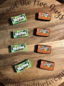 Four green boxes of "Sour Skittles" and four orange boxes of "Skittles Fruits" are neatly arranged on a wooden surface.