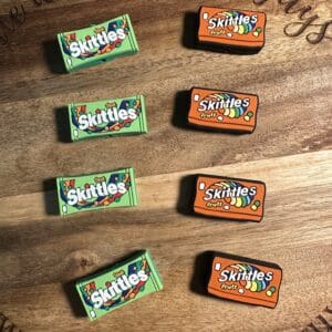 Four green boxes of "Sour Skittles" and four orange boxes of "Skittles Fruits" are neatly arranged on a wooden surface.