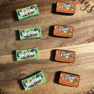 Four green boxes of "Sour Skittles" and four orange boxes of "Skittles Fruits" are neatly arranged on a wooden surface.