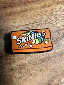 A small rubber keychain designed to look like a Skittles packet, placed on a wooden surface.