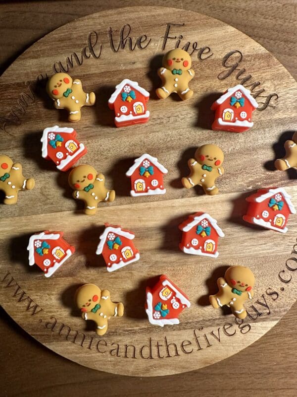 3D gingerbread man and house silicone focal beads displayed on a wooden platter.