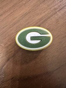 A Green Bay Silicone focal bead featuring a green G inside a yellow oval sits on a wooden surface.