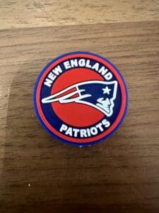 A Football silicone focal bead with the New England Patriots logo and team name on a red and blue background, placed on a wooden surface.