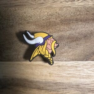 A small silicone focal bead featuring a Viking head with a yellow helmet and white horns, displayed on a wooden surface.