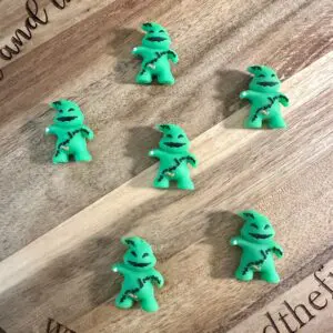 Six green, Oogie Boogie-themed 3D boogie focal beads are arranged on a round wooden board with the inscription "Around the Five Guys" and a website URL at the bottom.