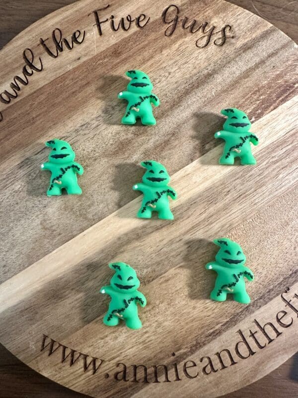 Six green, Oogie Boogie-themed 3D boogie focal beads are arranged on a round wooden board with the inscription "Around the Five Guys" and a website URL at the bottom.