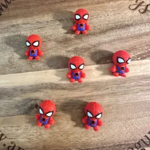 Six small 3D Spider-Man silicone focal beads are arranged on a wooden surface with engraved text around the edge.