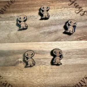 Five ET silicone focal beads featuring a character resembling an alien with a large head and big eyes are displayed on a wooden surface engraved with "annieandthefiveguys" and "Annie and the Five Guys.