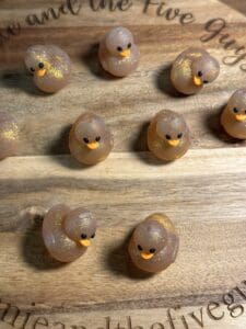 Ten "Ducks, 3D with golden sparkles" silicone focal beads are displayed on a wooden surface.