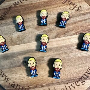 Round wooden board with the text "annie and the five guys" displaying nine small, illustrated Messi/soccer silicone focal beads depicting a bearded man with blond hair.