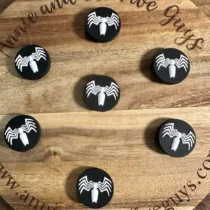 Round wooden board with the text "You're and the Five Guys" and a website at the bottom. Seven Venom silicone focal beads, featuring white spider logos, are arranged on the board.