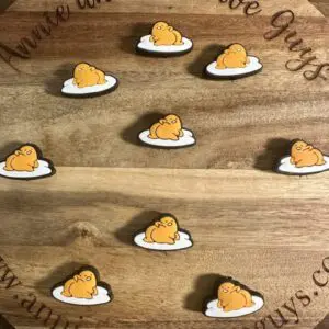 Wooden board displaying eight silicone focal beads depicting Gudetama, a resting yellow creature on a white cloud, arranged in a grid pattern. Text around the edges reads "Annie and the Five Guys" and a website address.