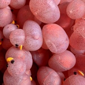 A cluster of speckled, translucent pink rubber ducks with small yellow beaks, piled together in a close-up view.