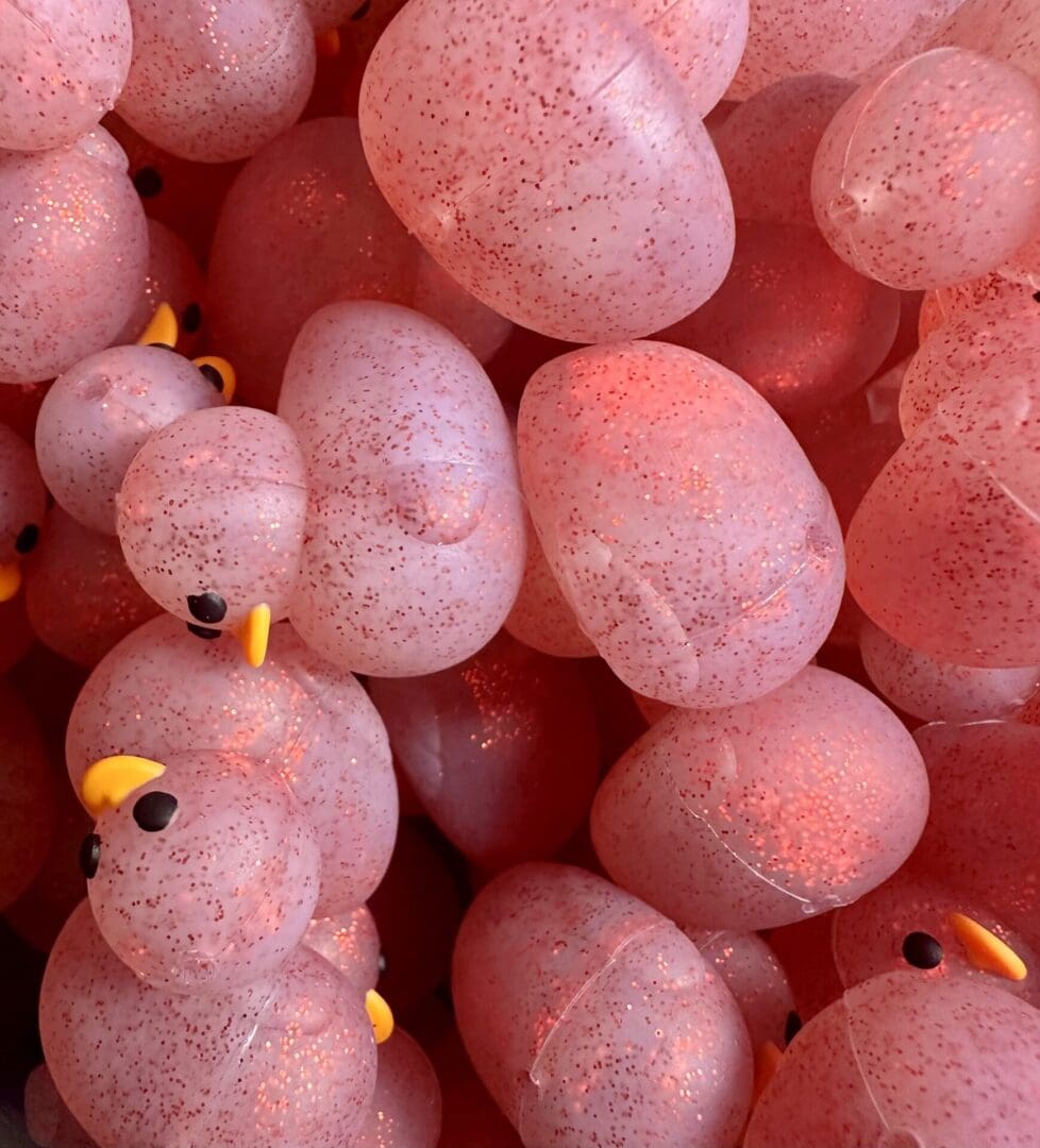 A cluster of speckled, translucent pink rubber ducks with small yellow beaks, piled together in a close-up view.