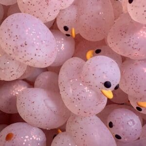 A close-up photo of many pink, translucent rubber ducks with black eyes and yellow beaks.