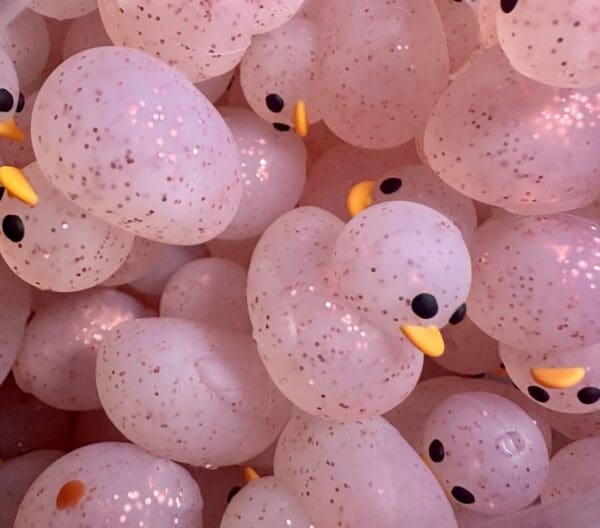 A close-up photo of many pink, translucent rubber ducks with black eyes and yellow beaks.