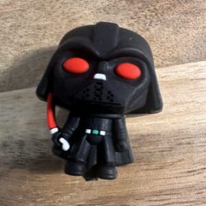 A 3D Darth Vader silicone focal bead, depicting a character in black armor and helmet with red eyes and wielding a red lightsaber, standing on a wooden surface.