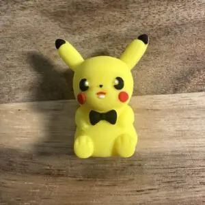 A small Pocket Monster Silicone Focal Bead 3D figurine of Pikachu with a black bowtie, sitting on a wooden surface.