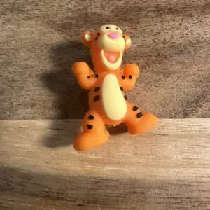 A 3D Tigger silicone focal bead, shaped like an orange tiger with black stripes and a cheerful expression, is standing on a wooden surface.