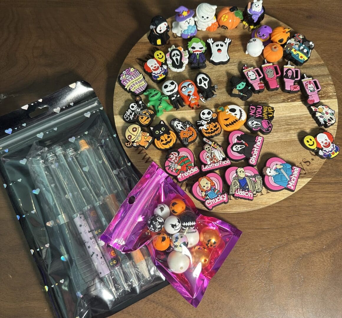 A wooden table showcases the Halloween Bundle, which includes an assortment of rubber charms and pins inspired by Halloween. To the left, two packages feature clear plastic pens and small balls, all adorned with Halloween themes.