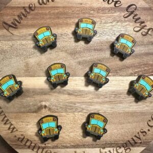 A wooden surface with a circular "Annie and the Five Guys" logo. Nine Magic School Bus silicone focal beads are arranged in a grid.