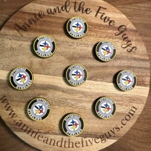 A wooden circular board with "Annie and the Five Guys" engraved on it, showcasing nine Pittsburgh football branded bottle caps arranged neatly in a pattern.