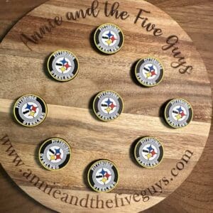 A wooden circular board with "Annie and the Five Guys" engraved on it, showcasing nine Pittsburgh football branded bottle caps arranged neatly in a pattern.