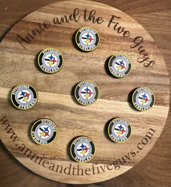 A wooden circular board with "Annie and the Five Guys" engraved on it, showcasing nine Pittsburgh football branded bottle caps arranged neatly in a pattern.