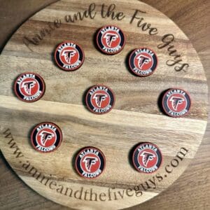 A wooden board displaying nine round coasters, each featuring an Atlanta football silicone focal bead with the Atlanta Falcons logo. The board is inscribed with "Annie and the Five Guys" and a website URL.